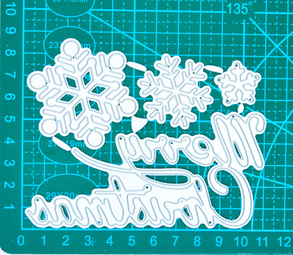 Merry Christmas and snowflake metal cutting dies on a centimetre cutting mat, showing the relative sizes of the four pieces.