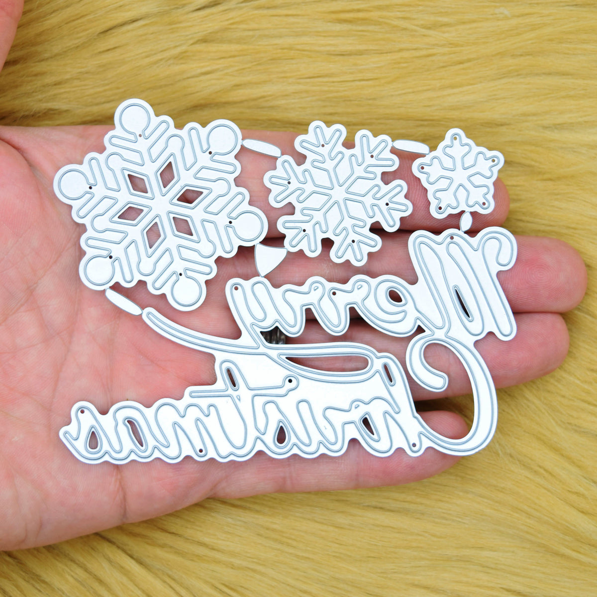 Large Merry Christmas and snowflake metal cutting dies held in a hand to show the size of the set.