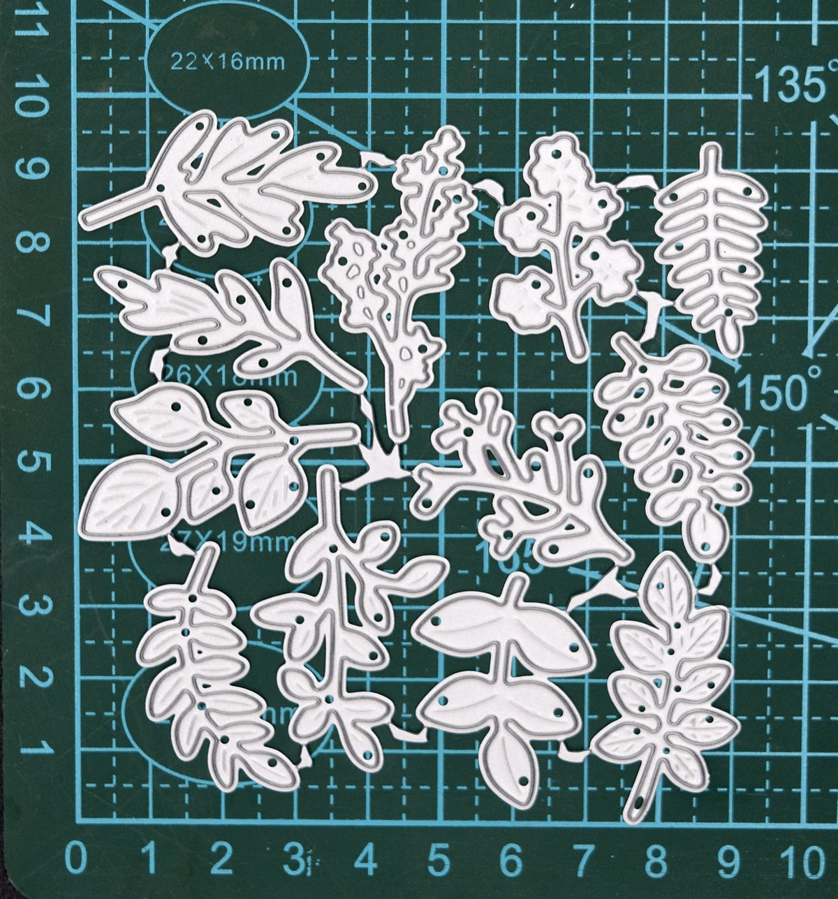 Connected leaf and foliage metal cutting dies displayed on a centimetre cutting mat for size reference