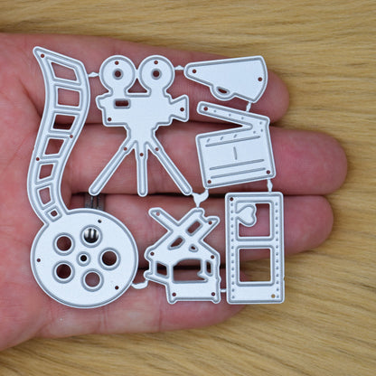 Movie themed metal cutting dies shown in hand for size reference including camera film reel and cinema accessory designs