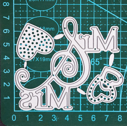 Mr and Mrs metal cutting dies with decorative ampersand and heart designs shown on cutting mat for size reference
