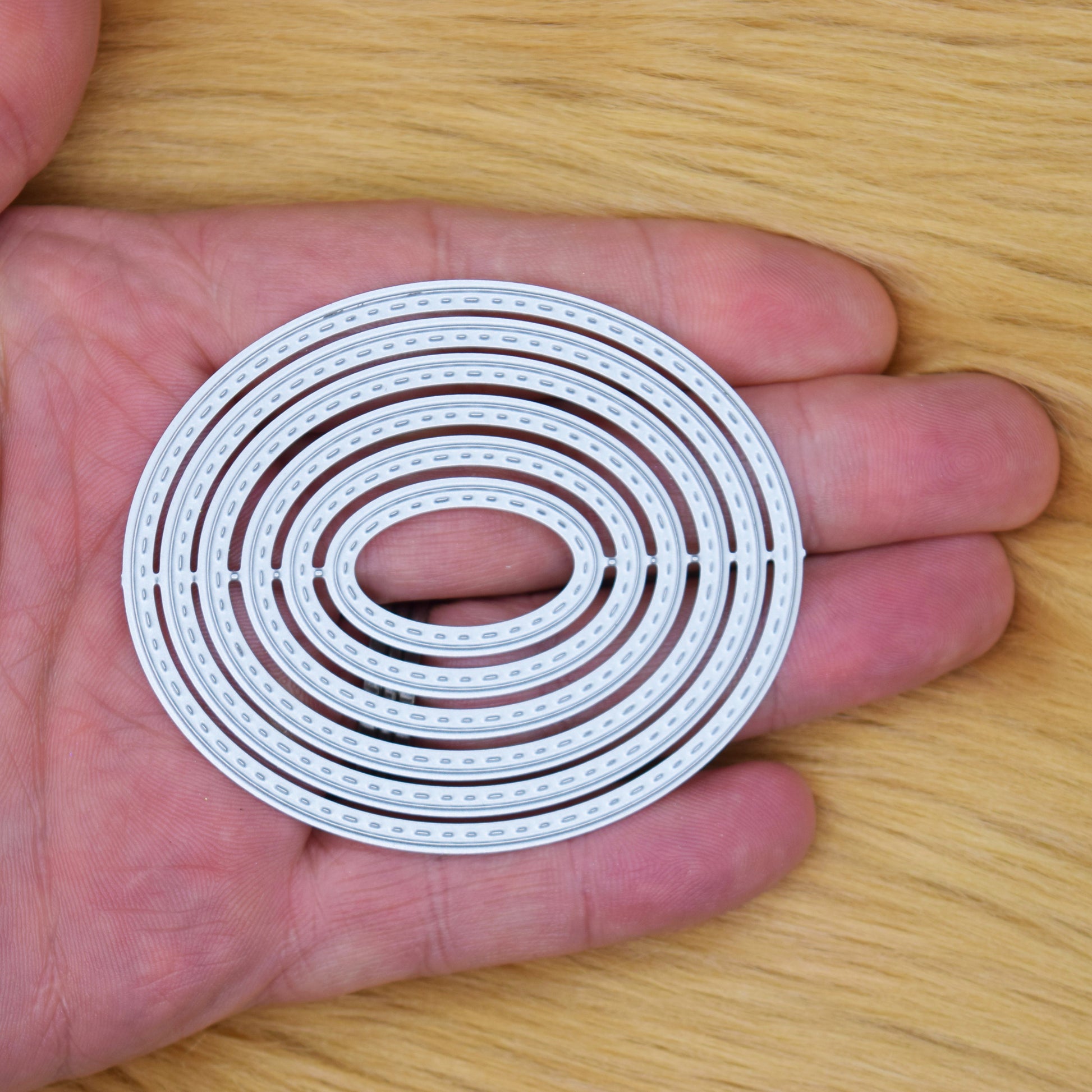 Set of 6 nesting stitched oval metal cutting dies held in hand to show size for card making
