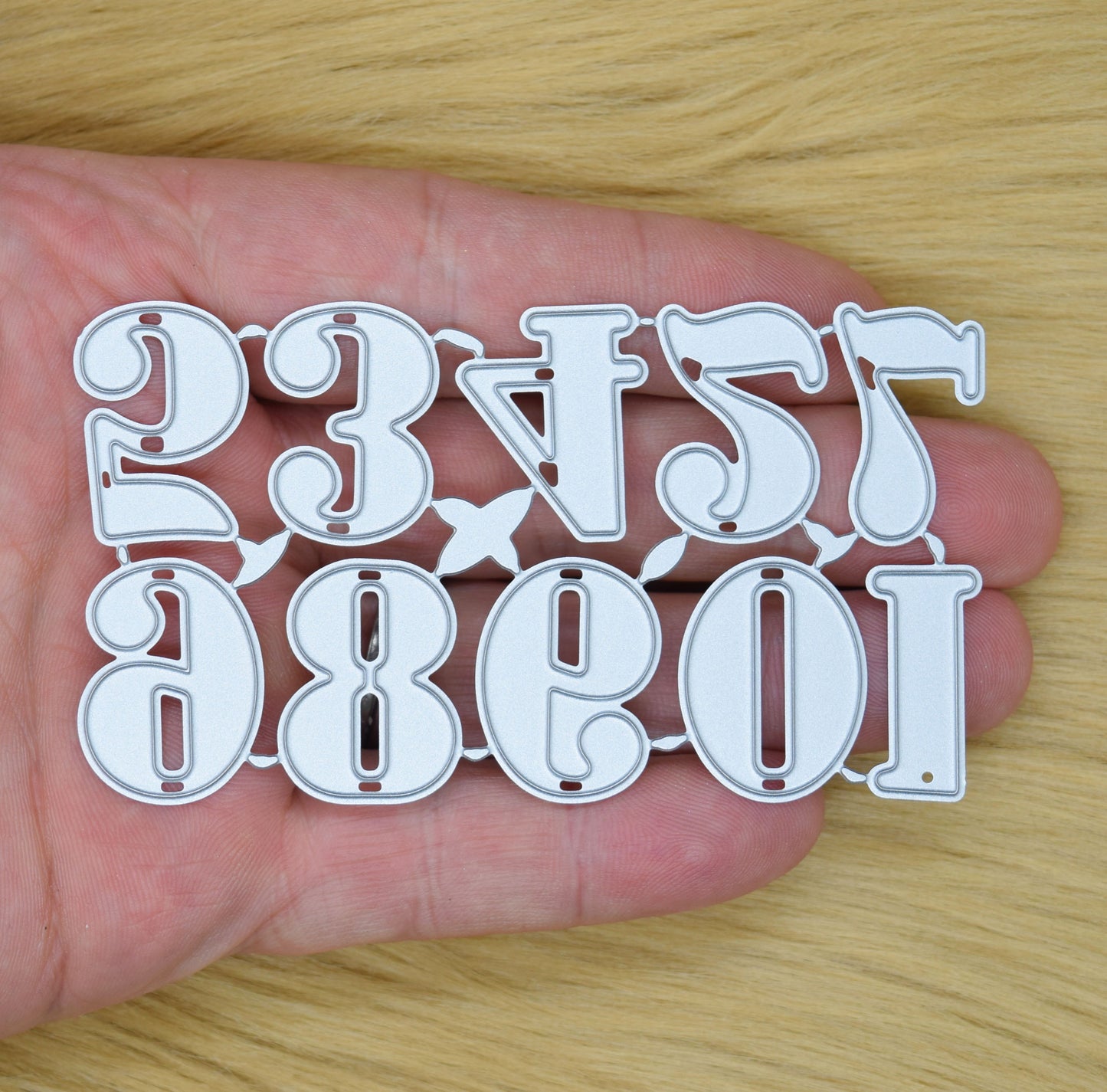 Decorative number metal cutting dies held in hand showing approximate size and detail