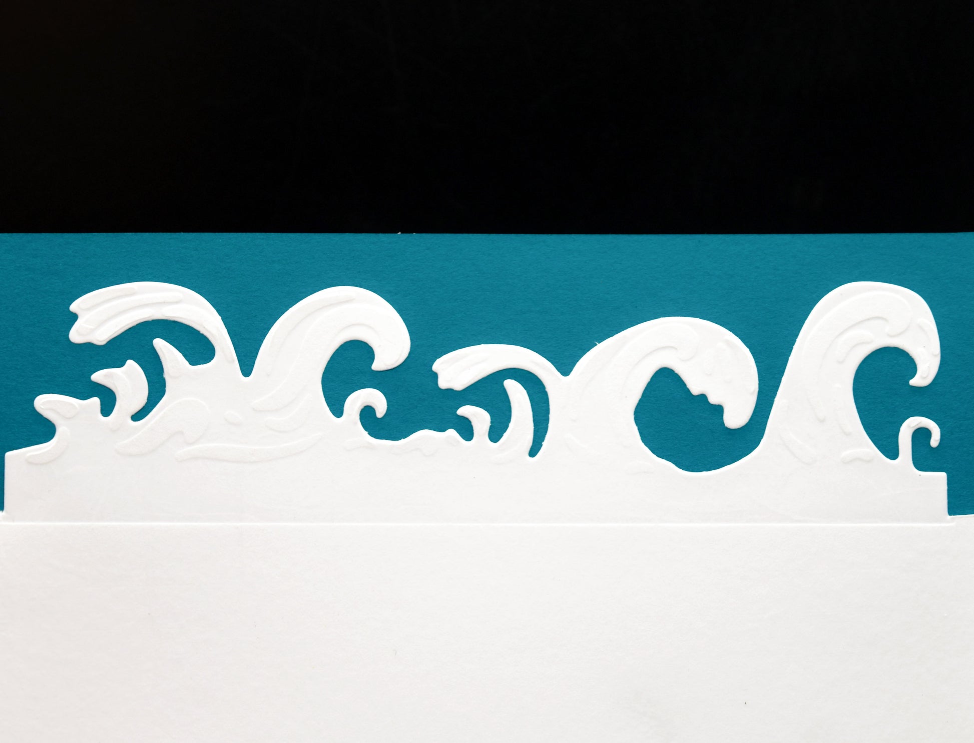 Finished ocean waves border cut made with the metal cutting die, shown in white card against blue and black background