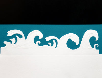 Finished ocean waves border cut made with the metal cutting die, shown in white card against blue and black background
