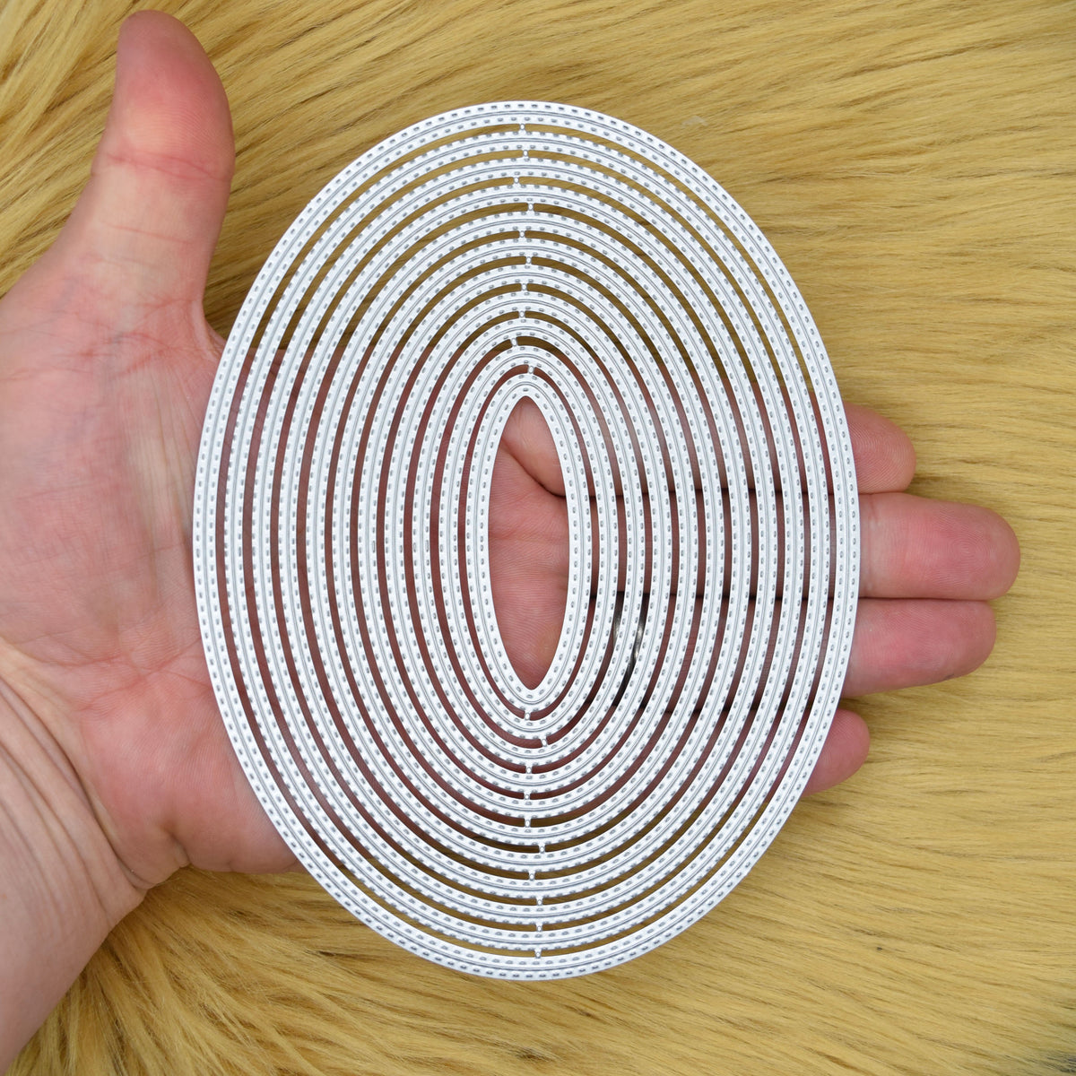 Large oval nesting metal cutting dies held in a hand to show the overall size of the set.