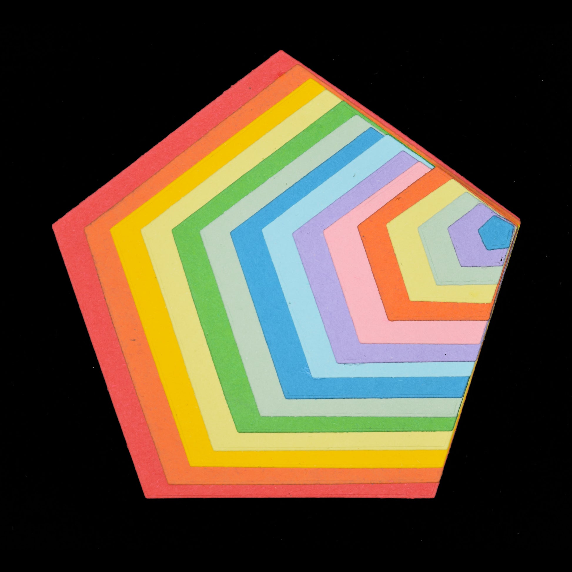 Graduated pentagon shapes cut from colourful card and layered together to demonstrate the 15 nesting metal cutting die sizes.