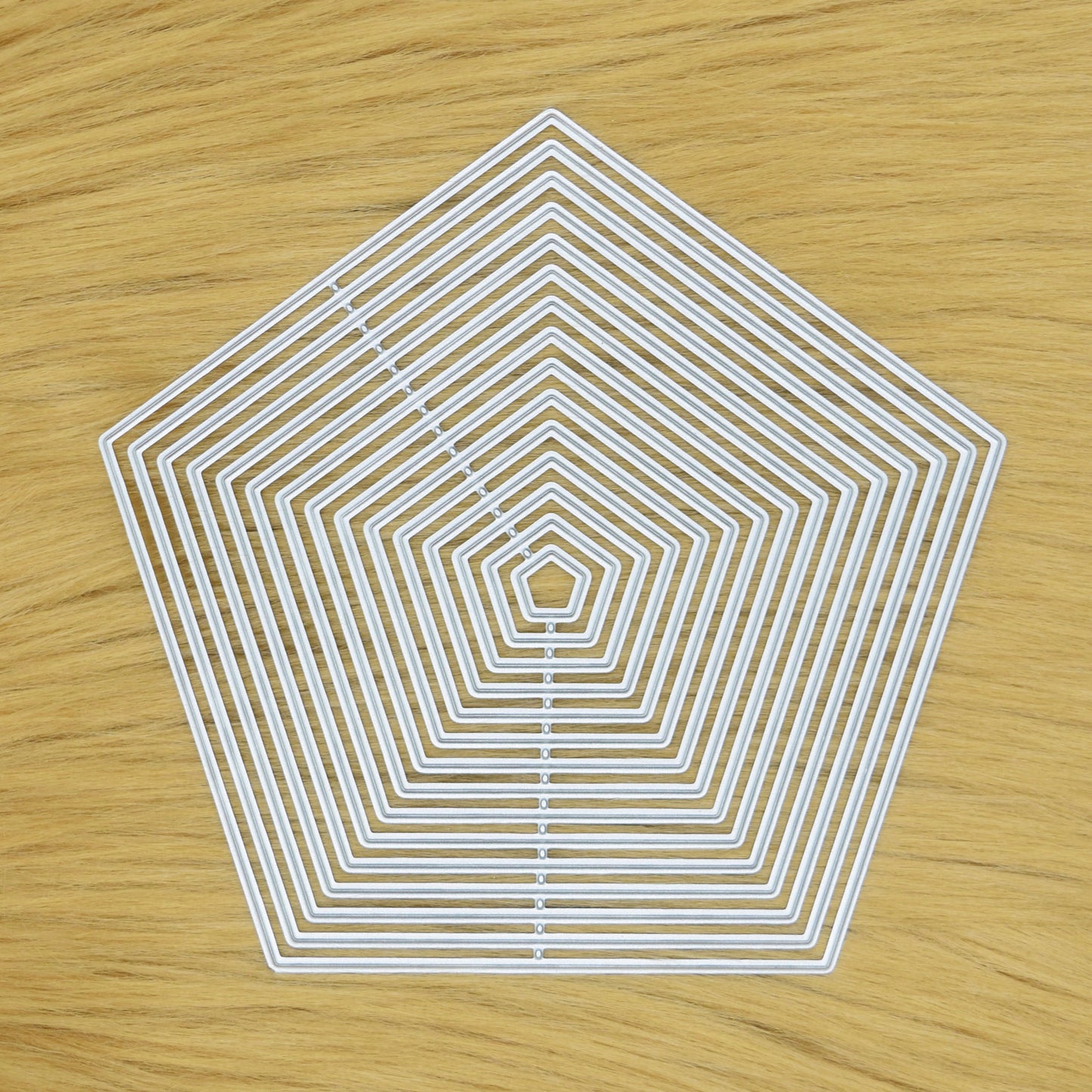 Set of 15 plain-edge pentagon nesting metal cutting dies displayed on a light faux fur background for card making and papercraft.