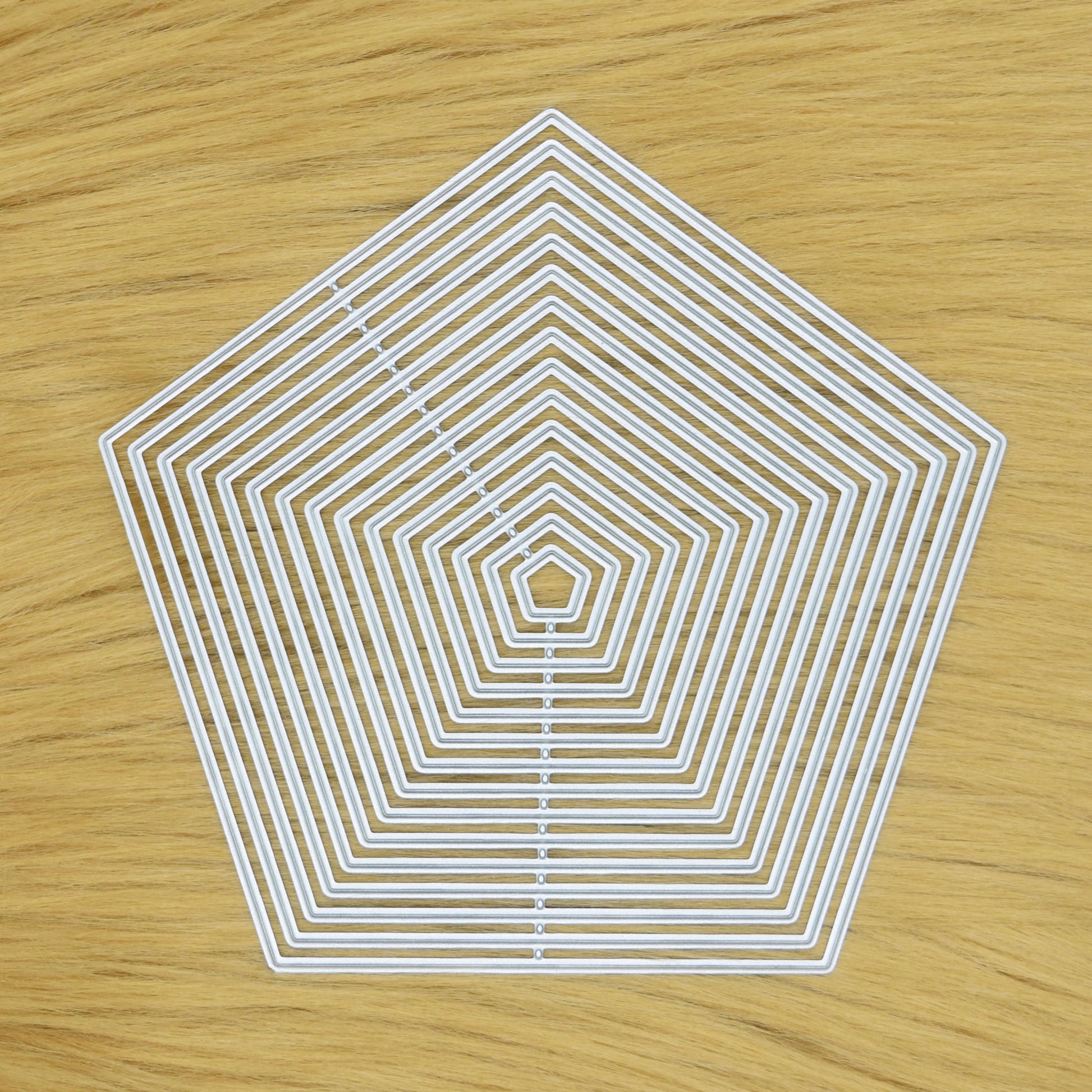 Set of 15 plain-edge pentagon nesting metal cutting dies displayed on a light faux fur background for card making and papercraft.