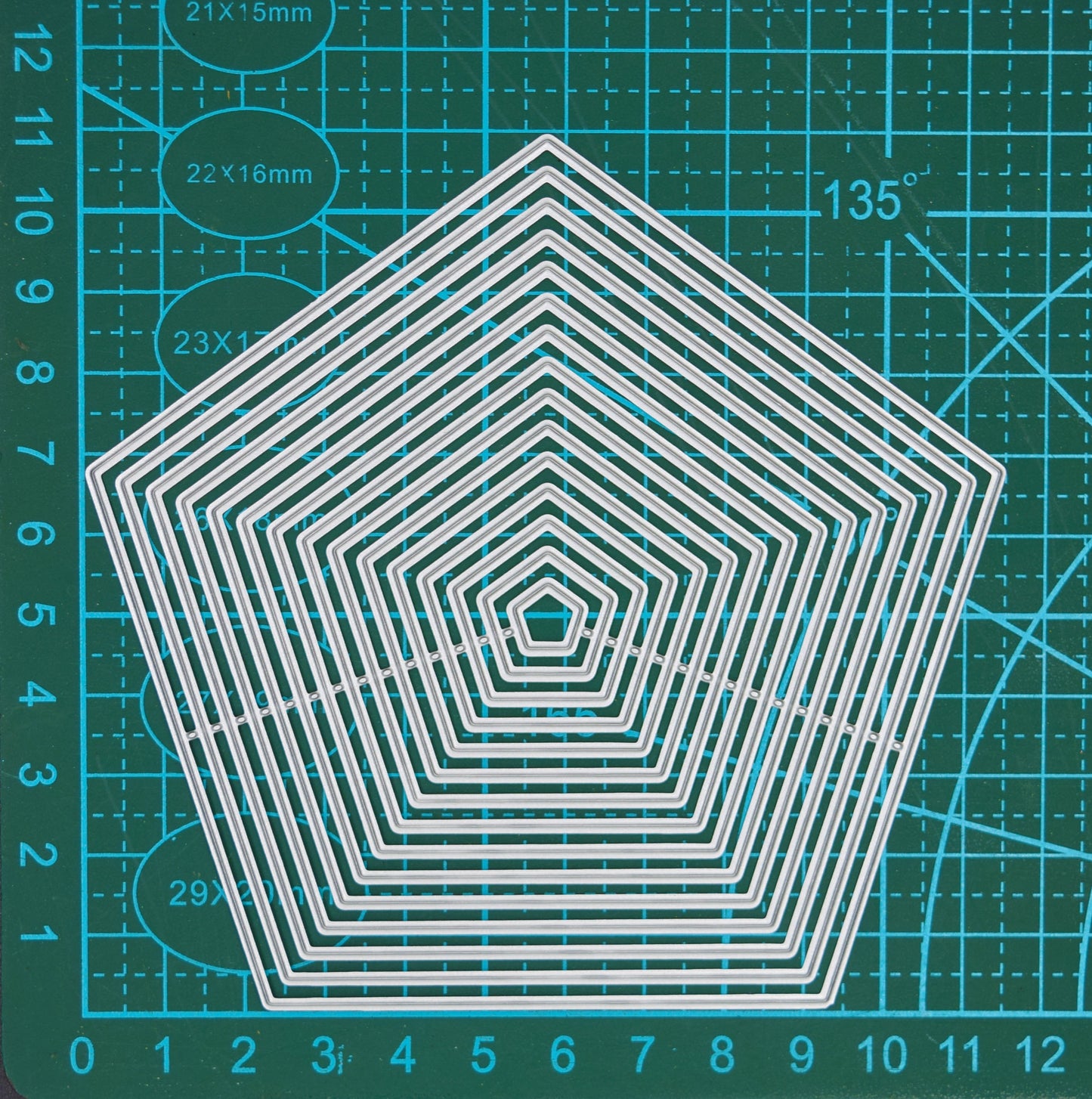 Pentagon nesting metal cutting dies displayed on a centimetre cutting mat to show the graduated sizes for card making and scrapbooking.