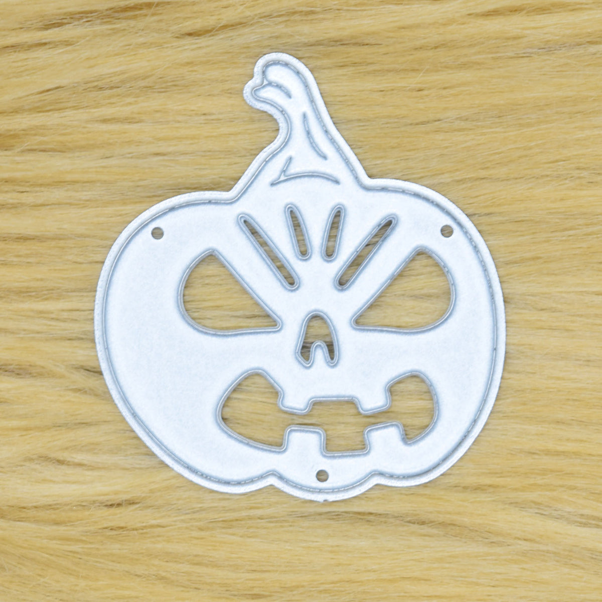 Halloween pumpkin metal cutting die displayed on a tan faux fur background for card making and papercraft.