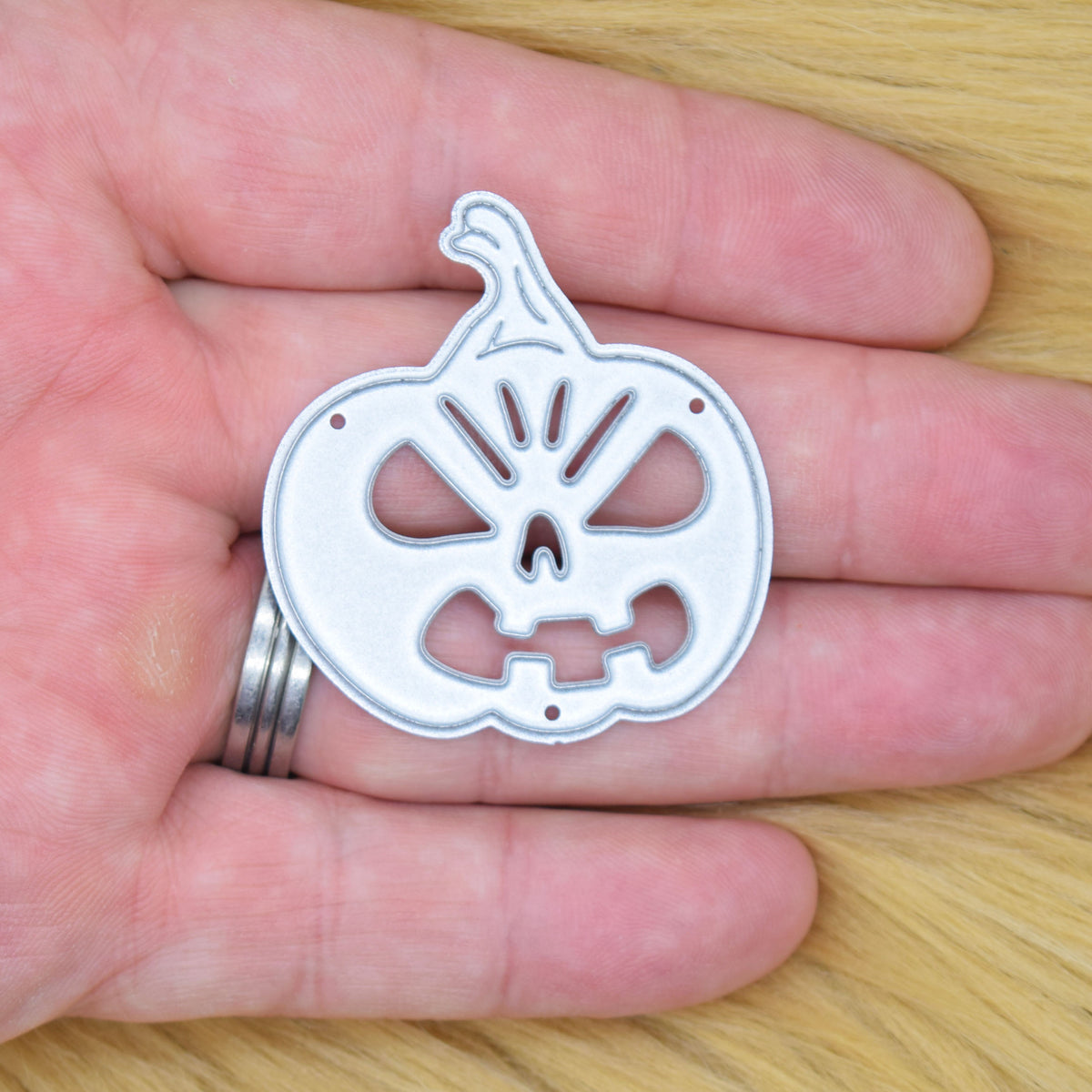 Jack o’ lantern pumpkin metal cutting die held in hand to show the approximate size of the die.