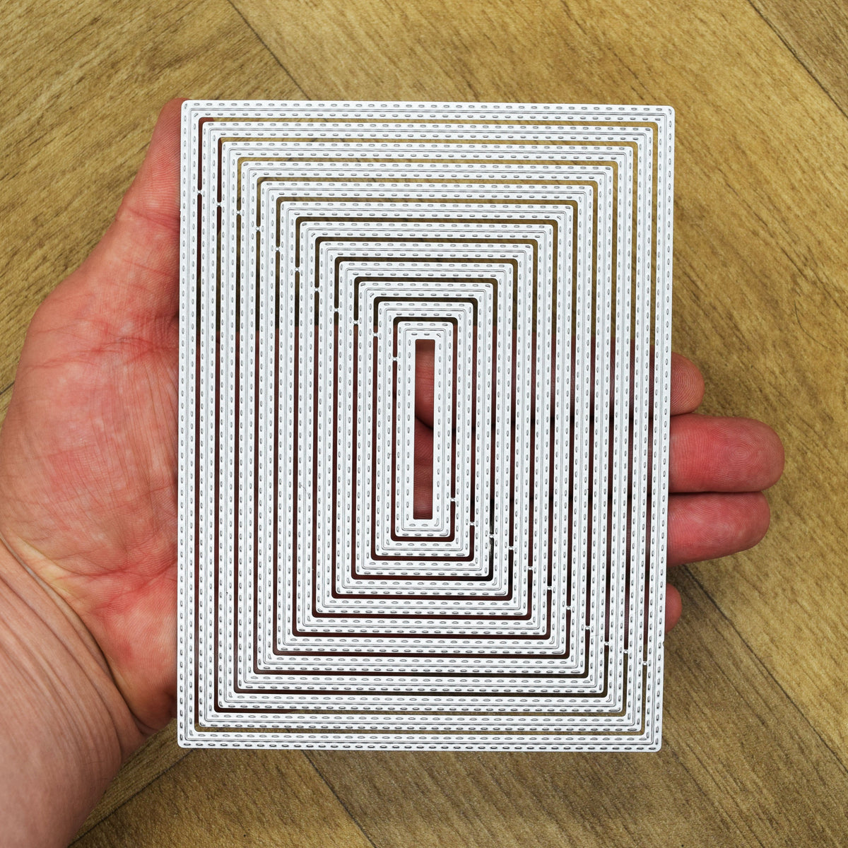 Twelve rectangle double stitched nesting metal cutting dies held in hand to demonstrate the overall size of the set