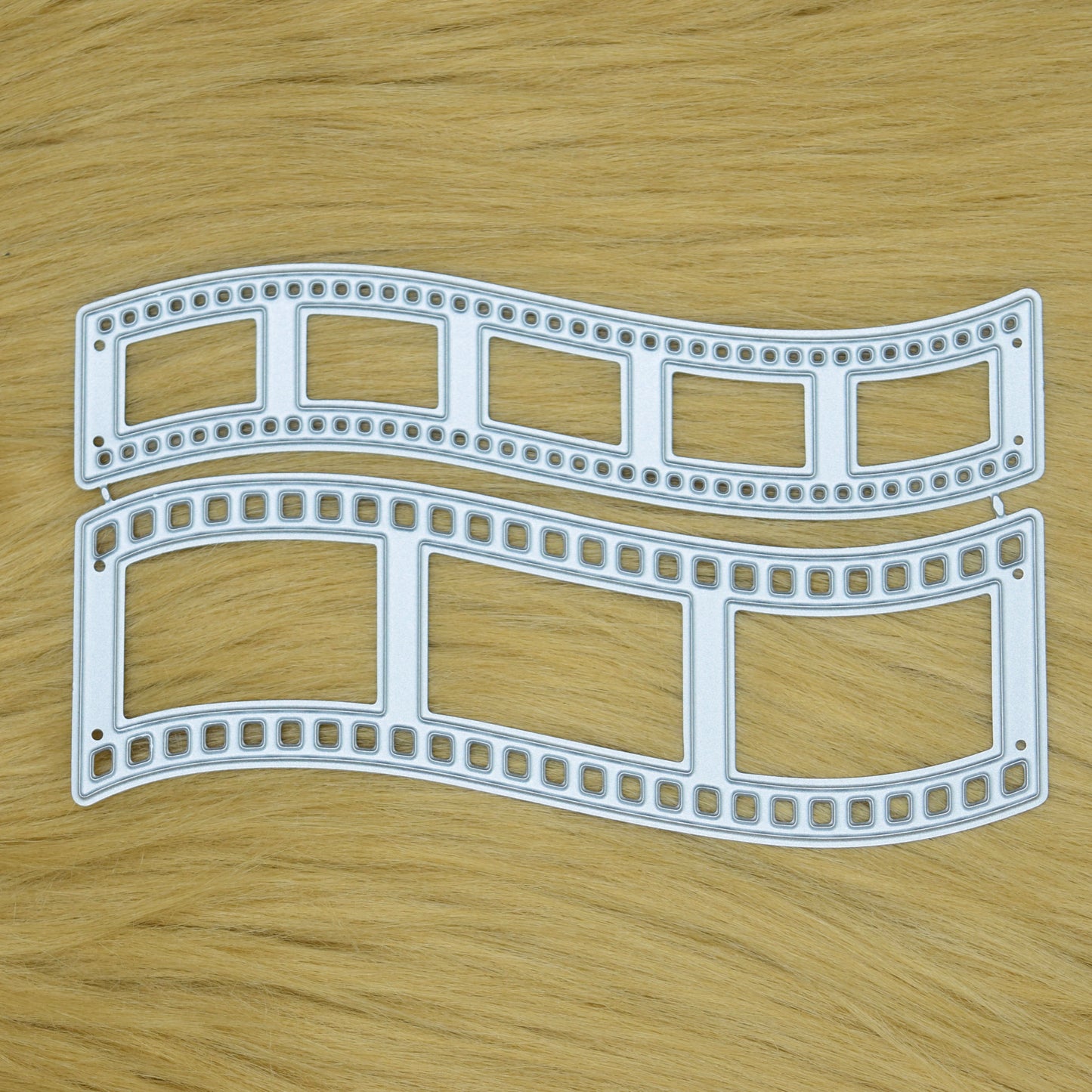 Two curved retro film strip metal cutting dies displayed on a faux fur background