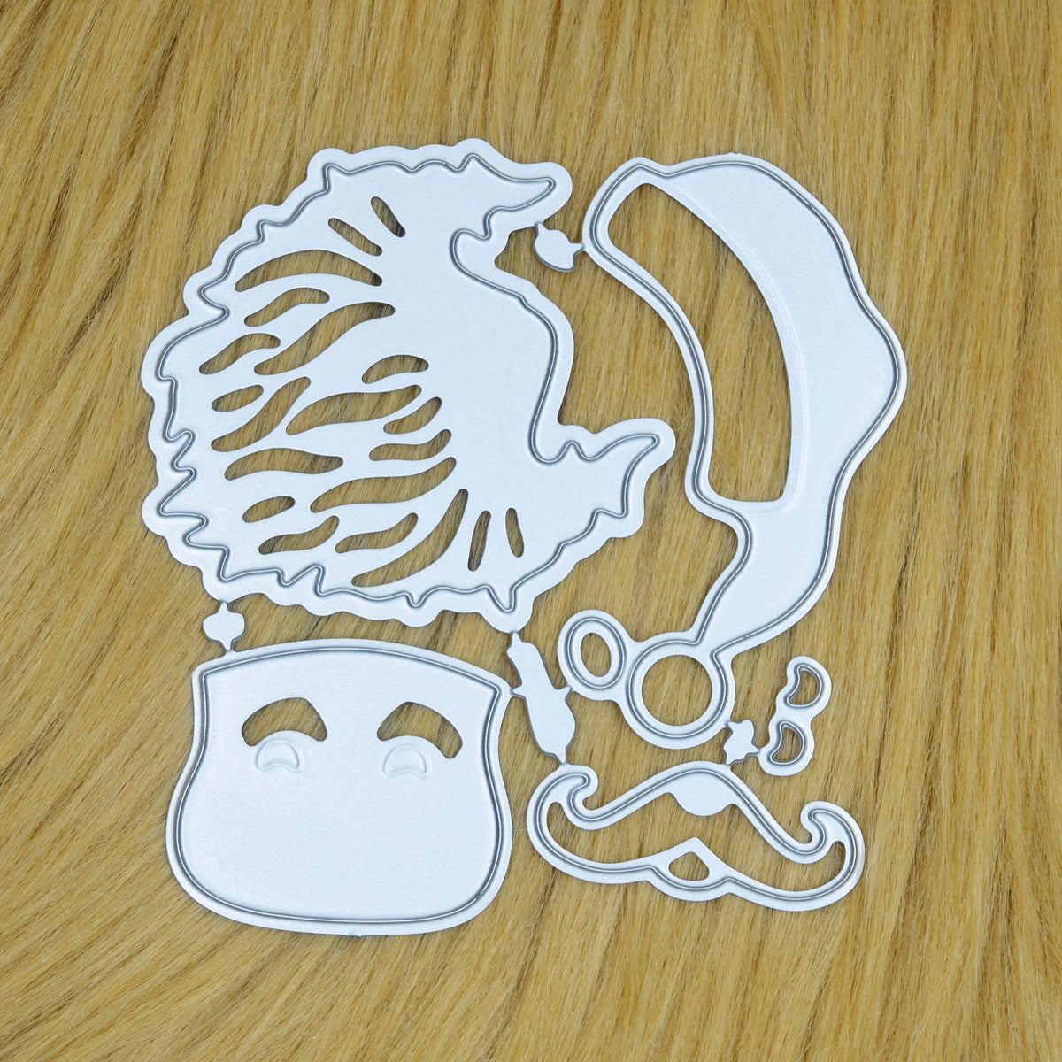 Santa face metal cutting dies on a tan faux fur background, showing the separate layering elements for Christmas card making.