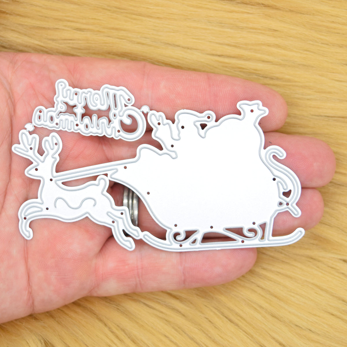 Santa sleigh and Merry Christmas metal cutting die set held in a hand to show its size for papercraft.