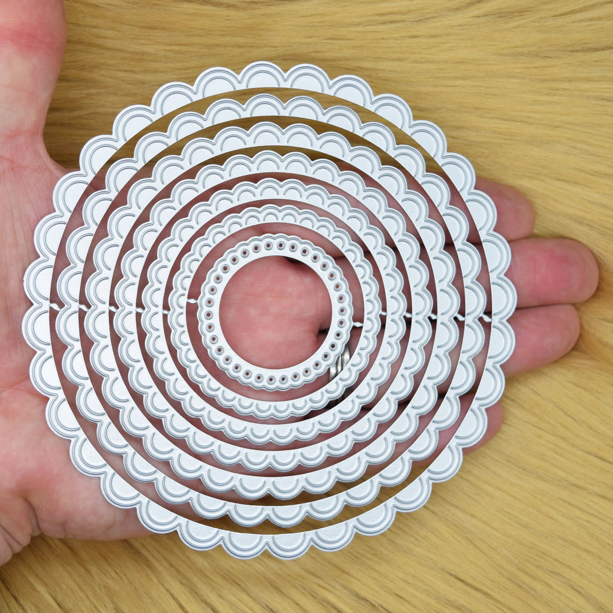 Scalloped circle nesting dies shown in hand for scale and size comparison