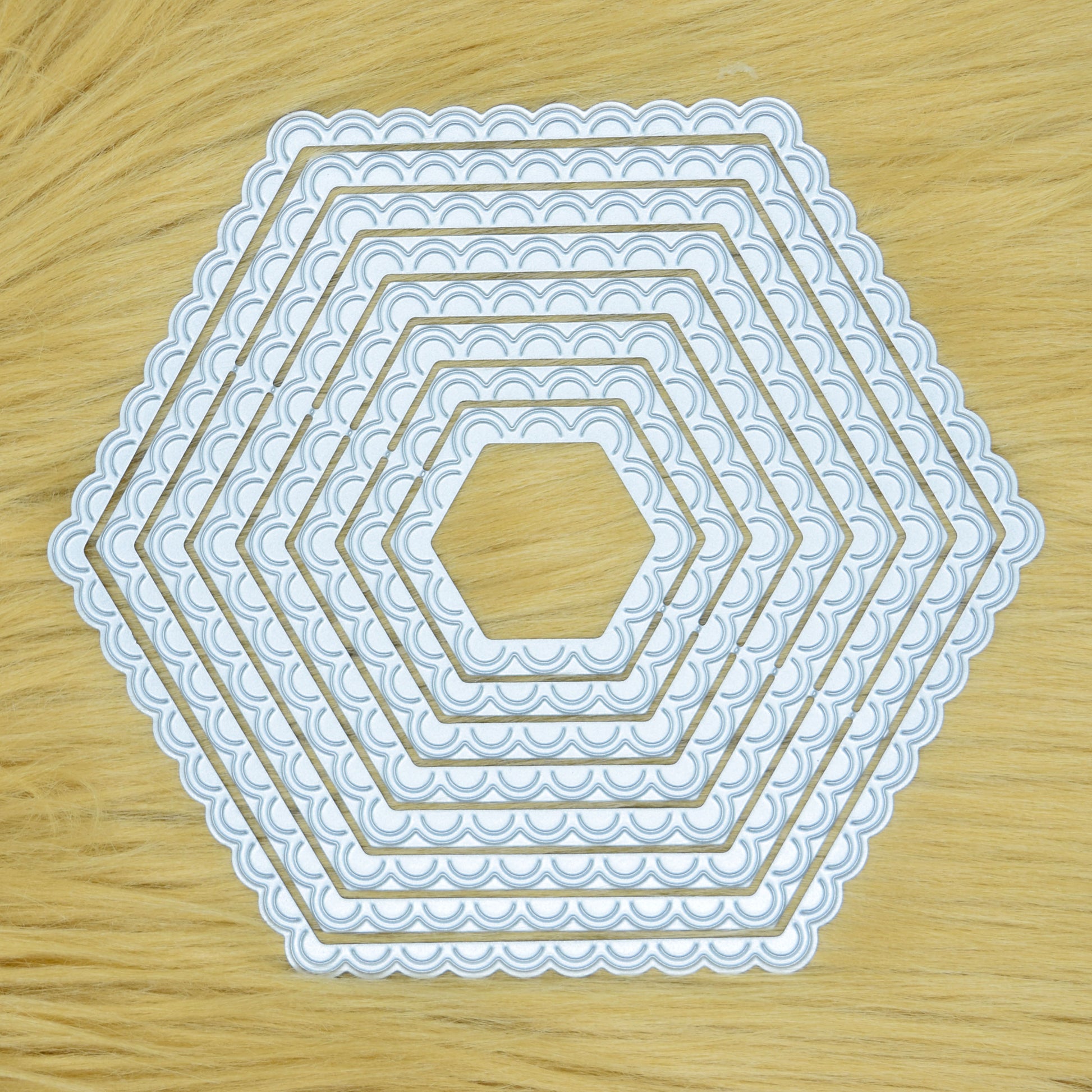 Graduated scalloped hexagon nesting metal cutting dies displayed on a light faux fur background for card making and papercraft.