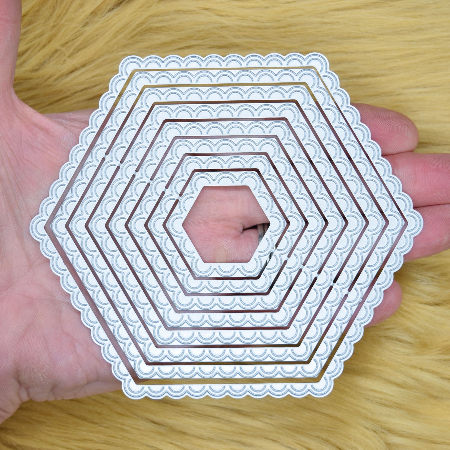 Scalloped hexagon nesting metal cutting dies shown in hand to demonstrate the graduated sizes and decorative edges.