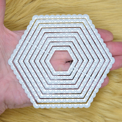 Scalloped hexagon nesting metal cutting dies shown in hand to demonstrate the graduated sizes and decorative edges.