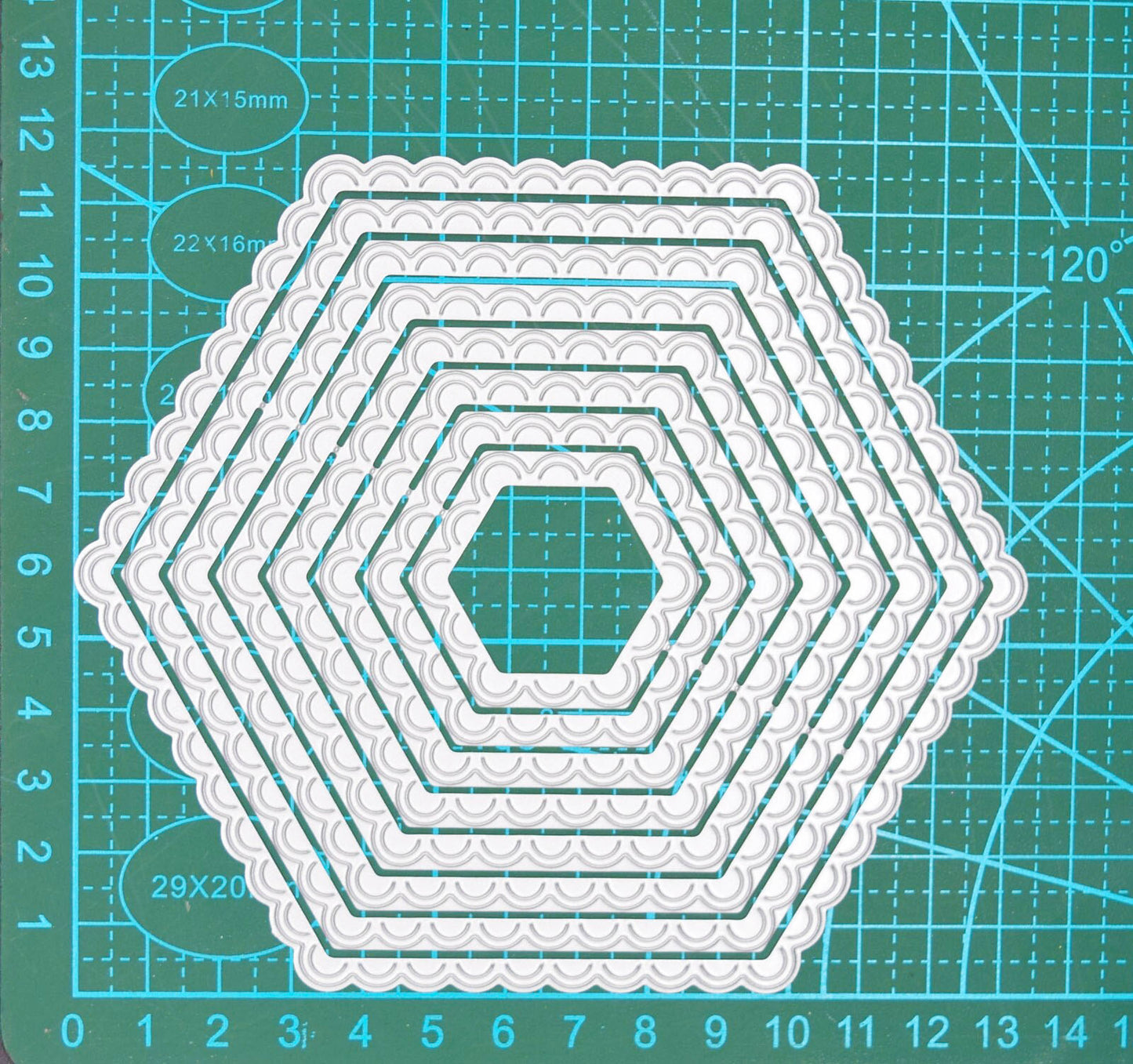 Graduated scalloped hexagon nesting metal cutting dies displayed on a centimetre cutting mat to demonstrate their sizes.