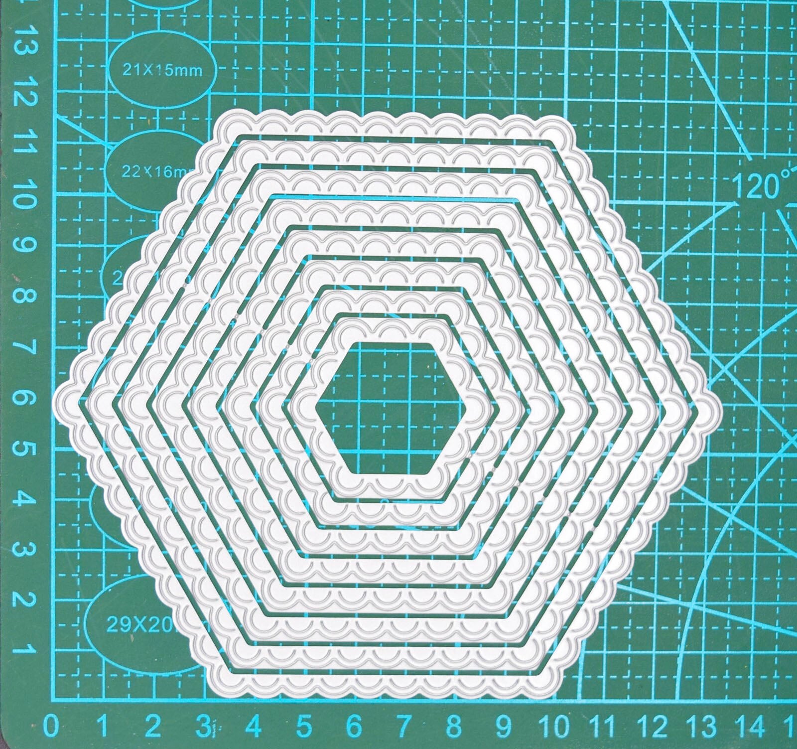 Graduated scalloped hexagon nesting metal cutting dies displayed on a centimetre cutting mat to demonstrate their sizes.
