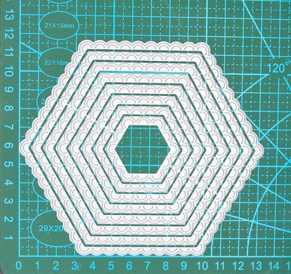 Graduated scalloped hexagon nesting metal cutting dies displayed on a centimetre cutting mat to demonstrate their sizes.