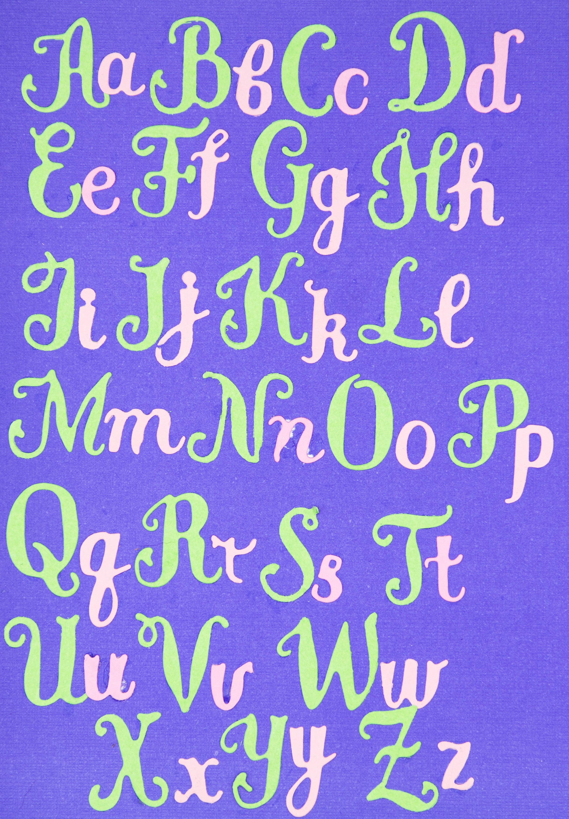 Decorative uppercase and lowercase script alphabet cuts arranged on purple cardstock for card making and papercraft