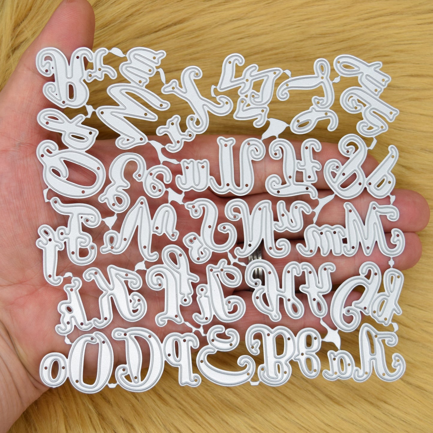 Connected uppercase and lowercase script alphabet metal cutting die set held in hand to demonstrate its overall size