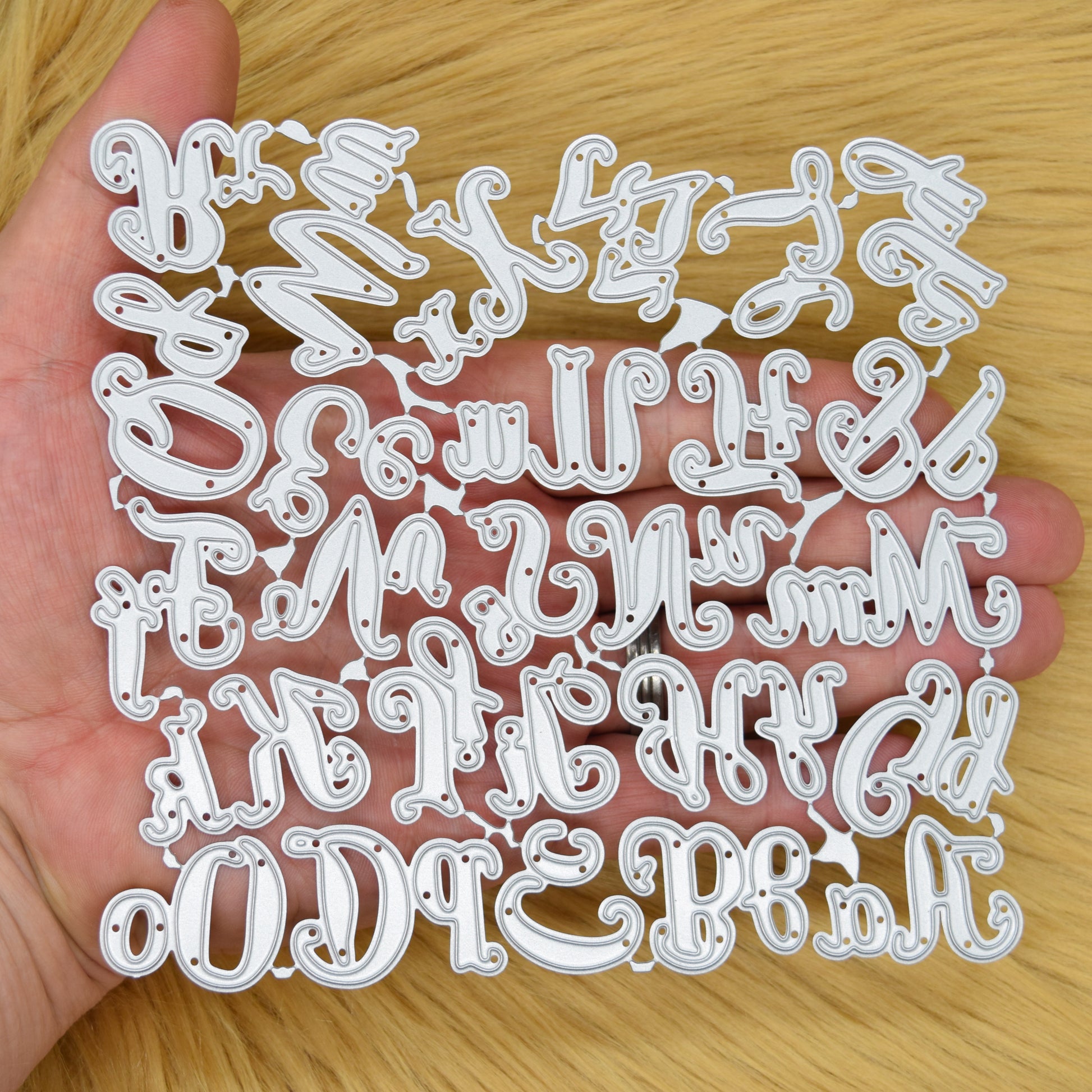 Connected uppercase and lowercase script alphabet metal cutting die set held in hand to demonstrate its overall size