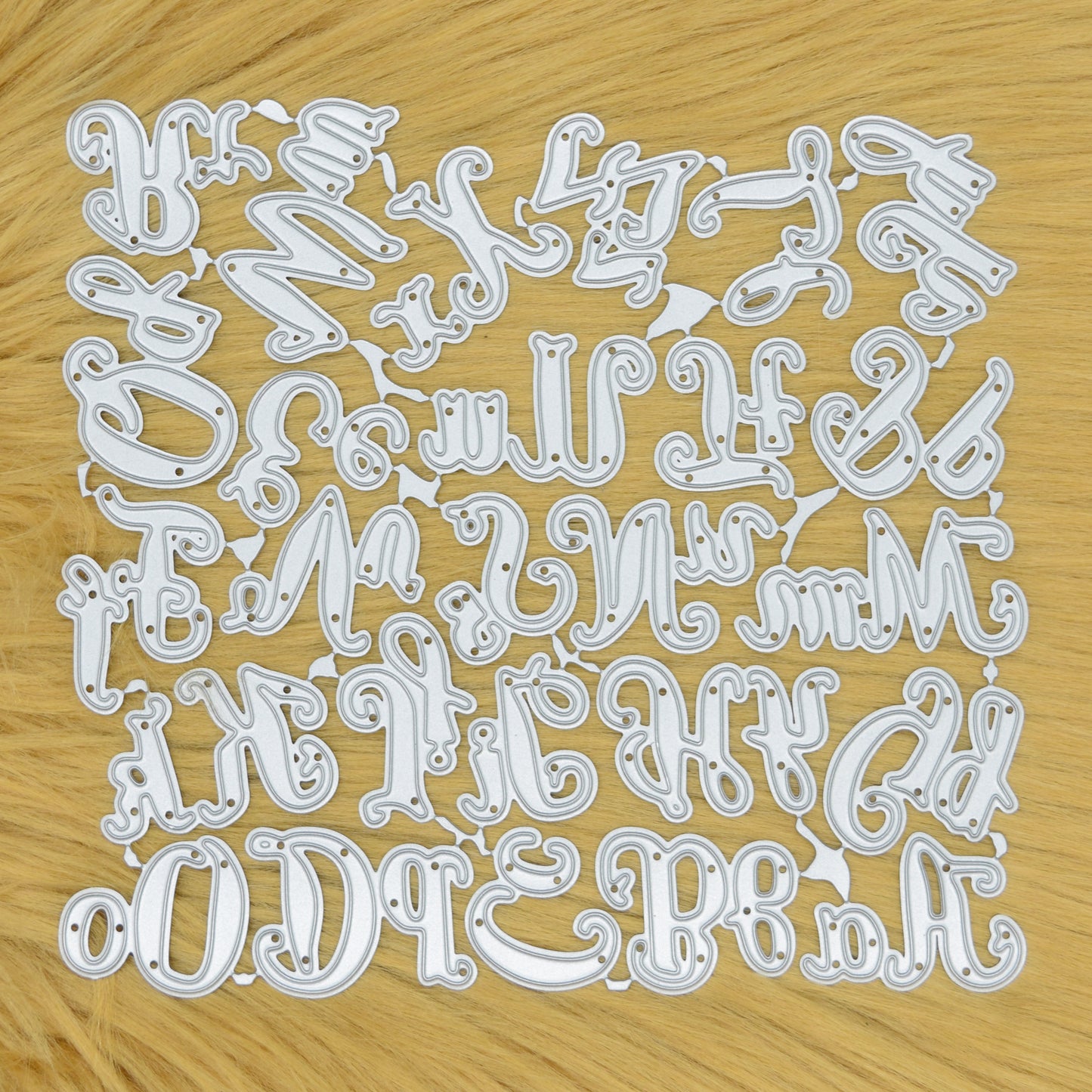 Uppercase and lowercase script alphabet metal cutting dies displayed connected on a light tan faux fur background
