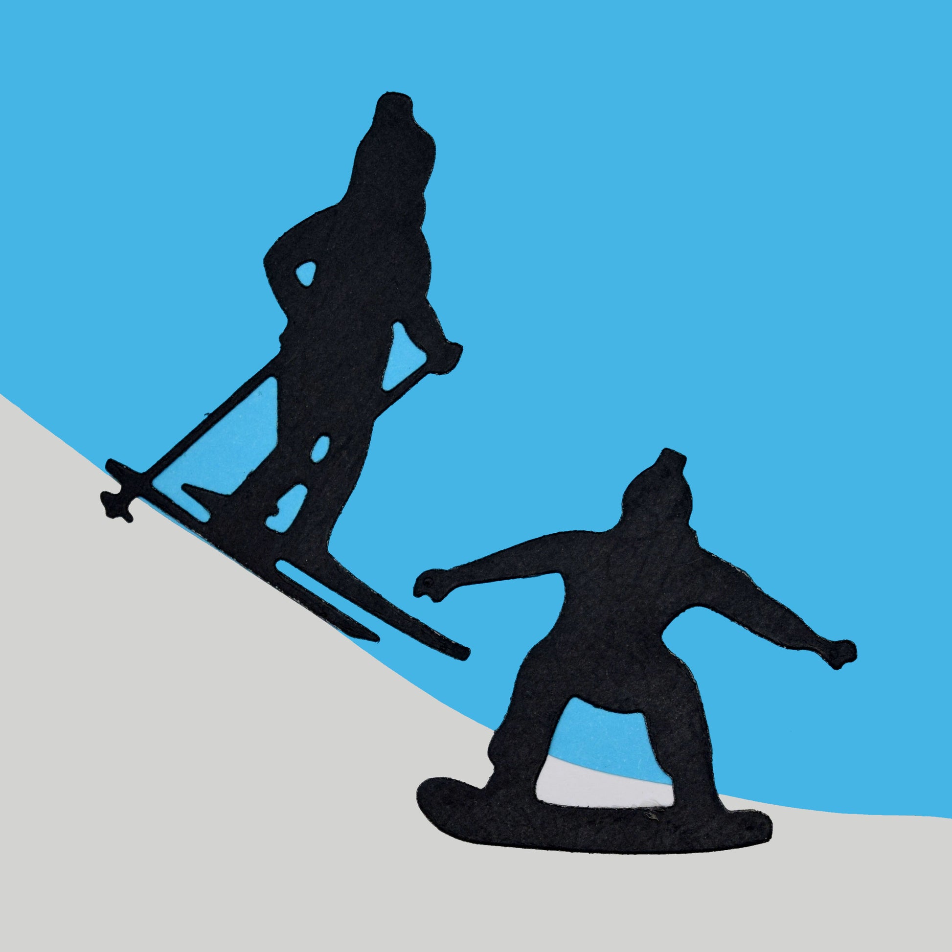 Black skier and snowboarder die cuts arranged on a blue and white snowy background for winter sports cards and scrapbook projects.
