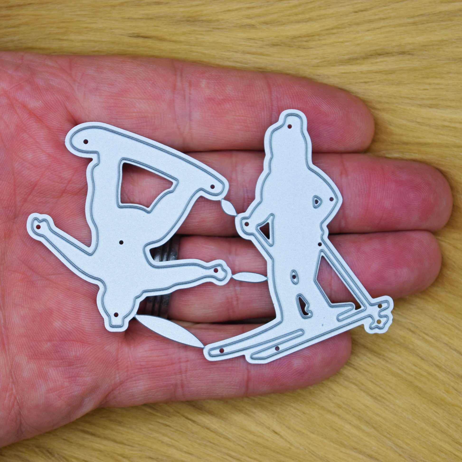 Skier and snowboarder metal cutting dies shown in hand to demonstrate their size for handmade cards and winter papercraft.