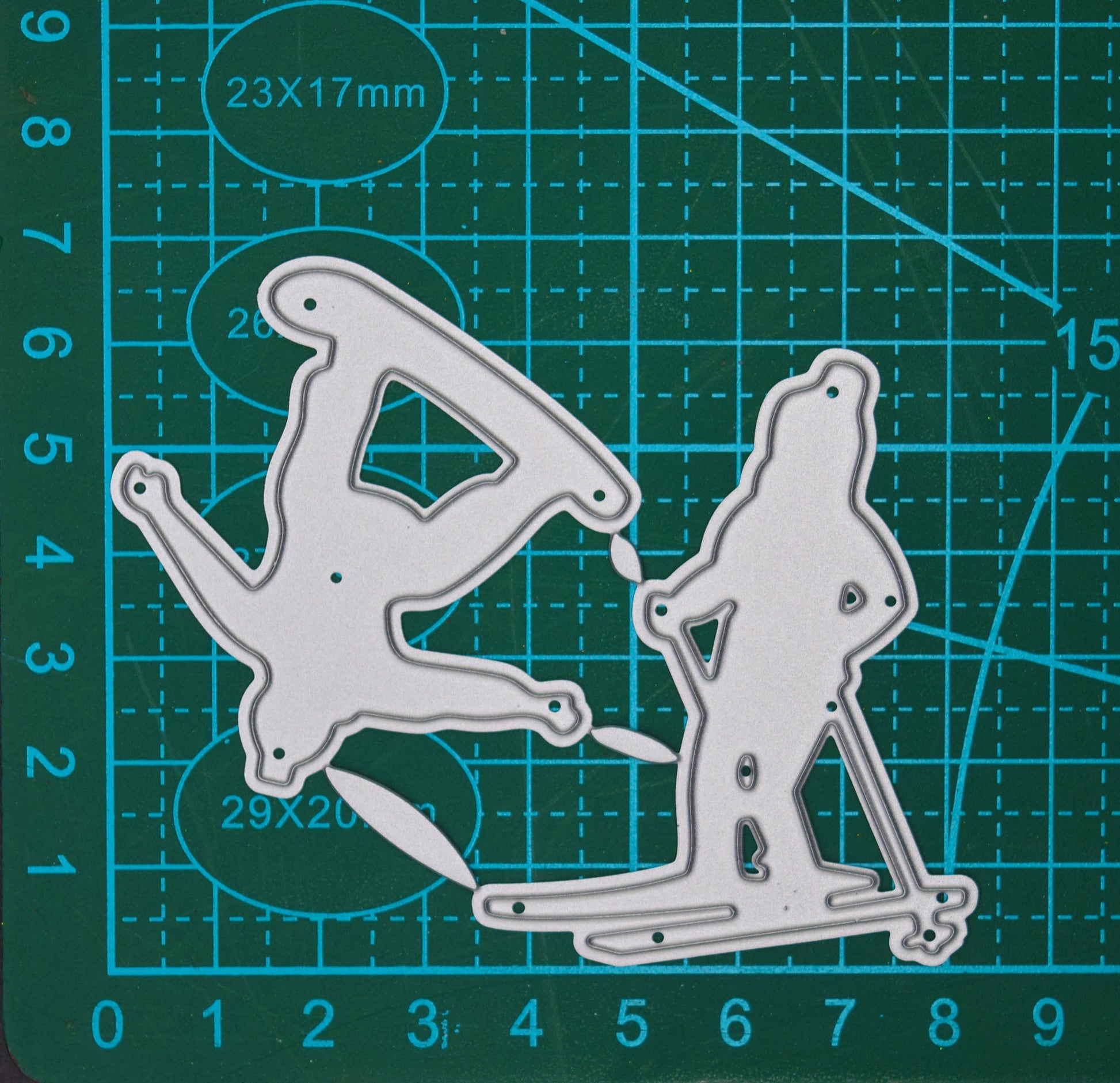 Skier and snowboarder metal cutting dies displayed on a centimetre cutting mat to show their size for winter card making and papercraft.