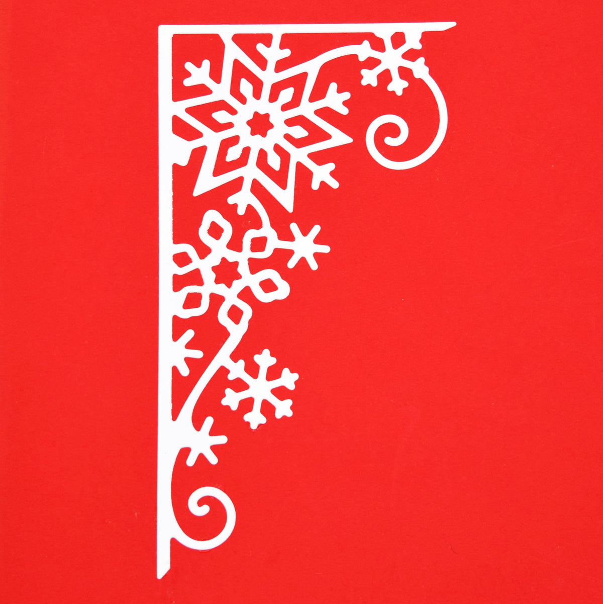 White snowflake corner border paper cut on red card, showing the decorative Christmas design created with the metal cutting die.
