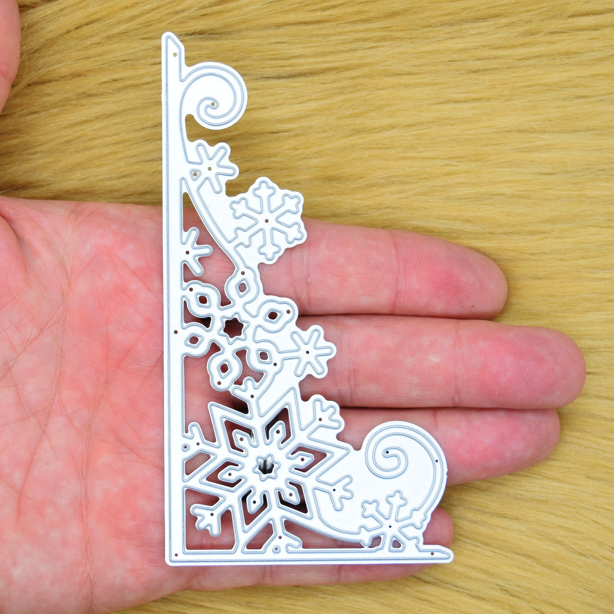 Christmas snowflake corner border metal cutting die held in hand to show its large size and detailed design.