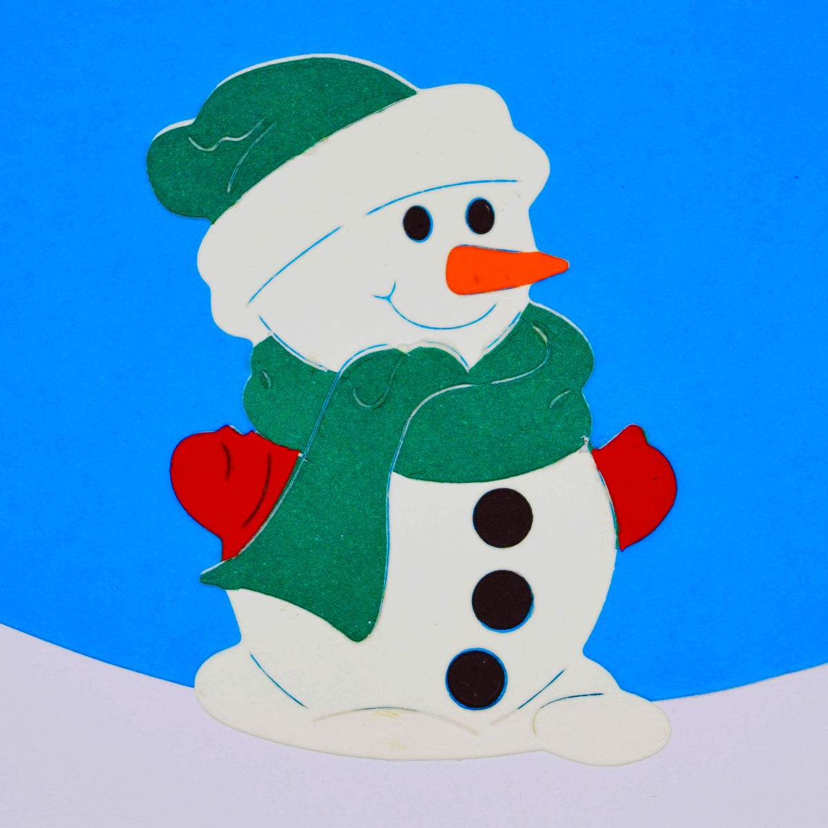Coloured snowman paper cut with a green hat and scarf, red mittens and black buttons against a blue and white snowy background.