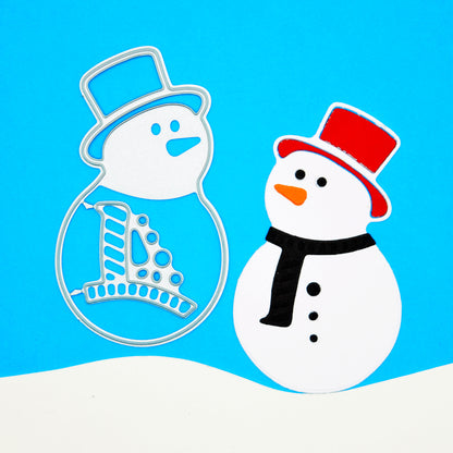 Snowman metal cutting dies beside a finished paper snowman on a blue background with a white snowbank for Christmas card making.