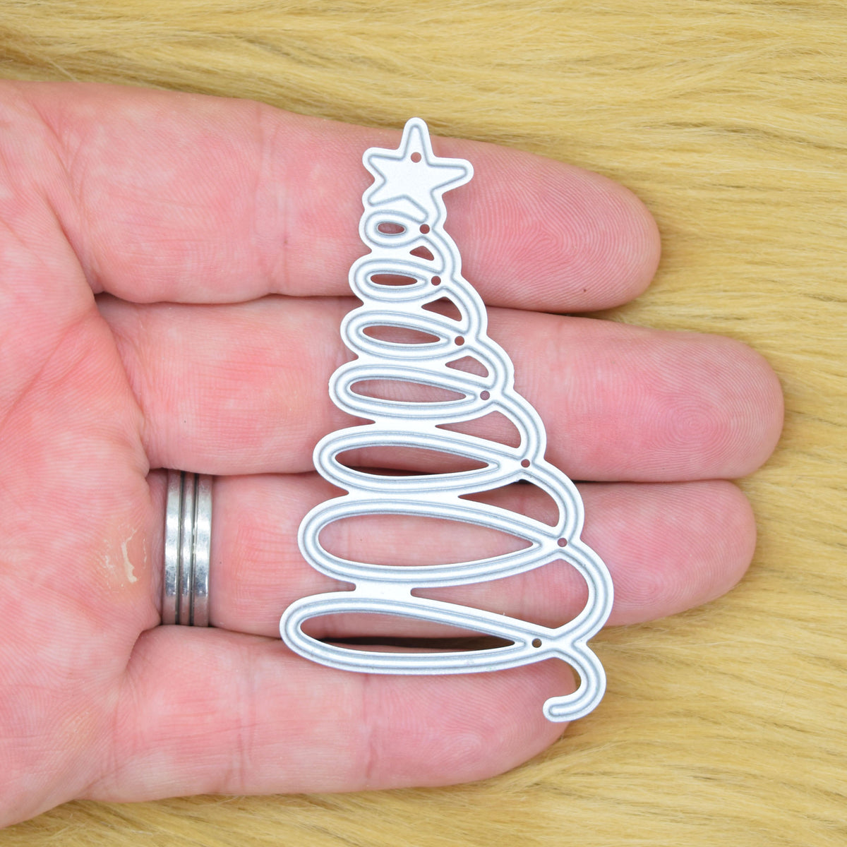 Spiral Christmas tree metal cutting die held in hand to show the overall size of the modern festive design.