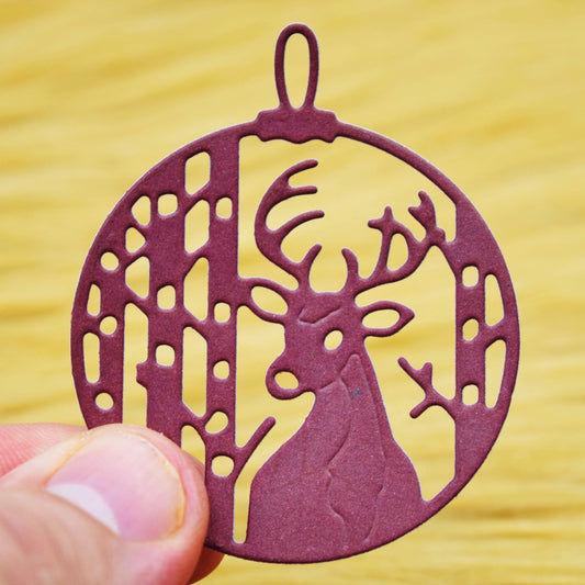 Burgundy paper stag bauble held between fingers, showing woodland cut-out details and embossed lines made with the metal cutting die.