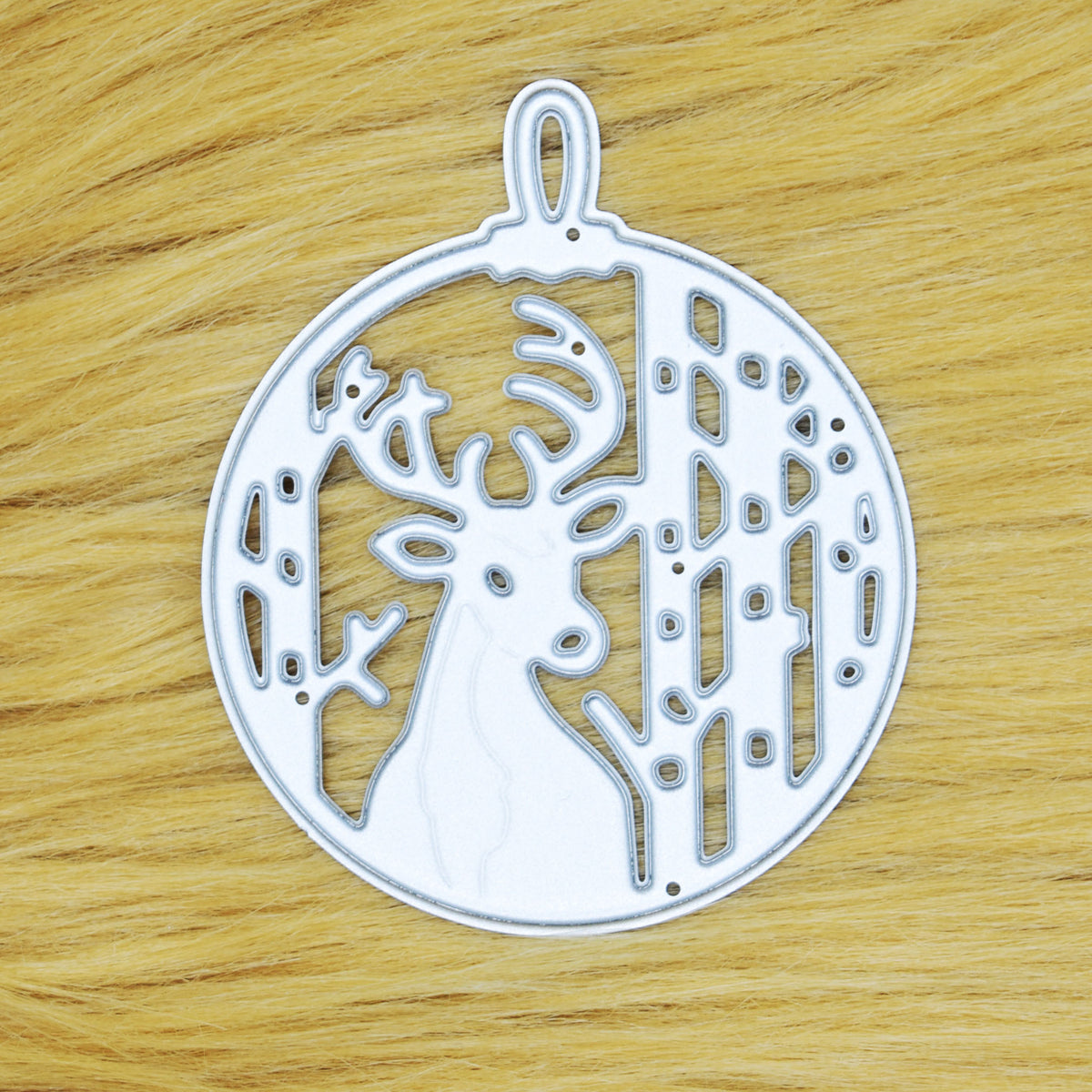 Stag Christmas bauble metal cutting die on a tan faux fur background, showing the deer, trees and hanging loop for papercraft.