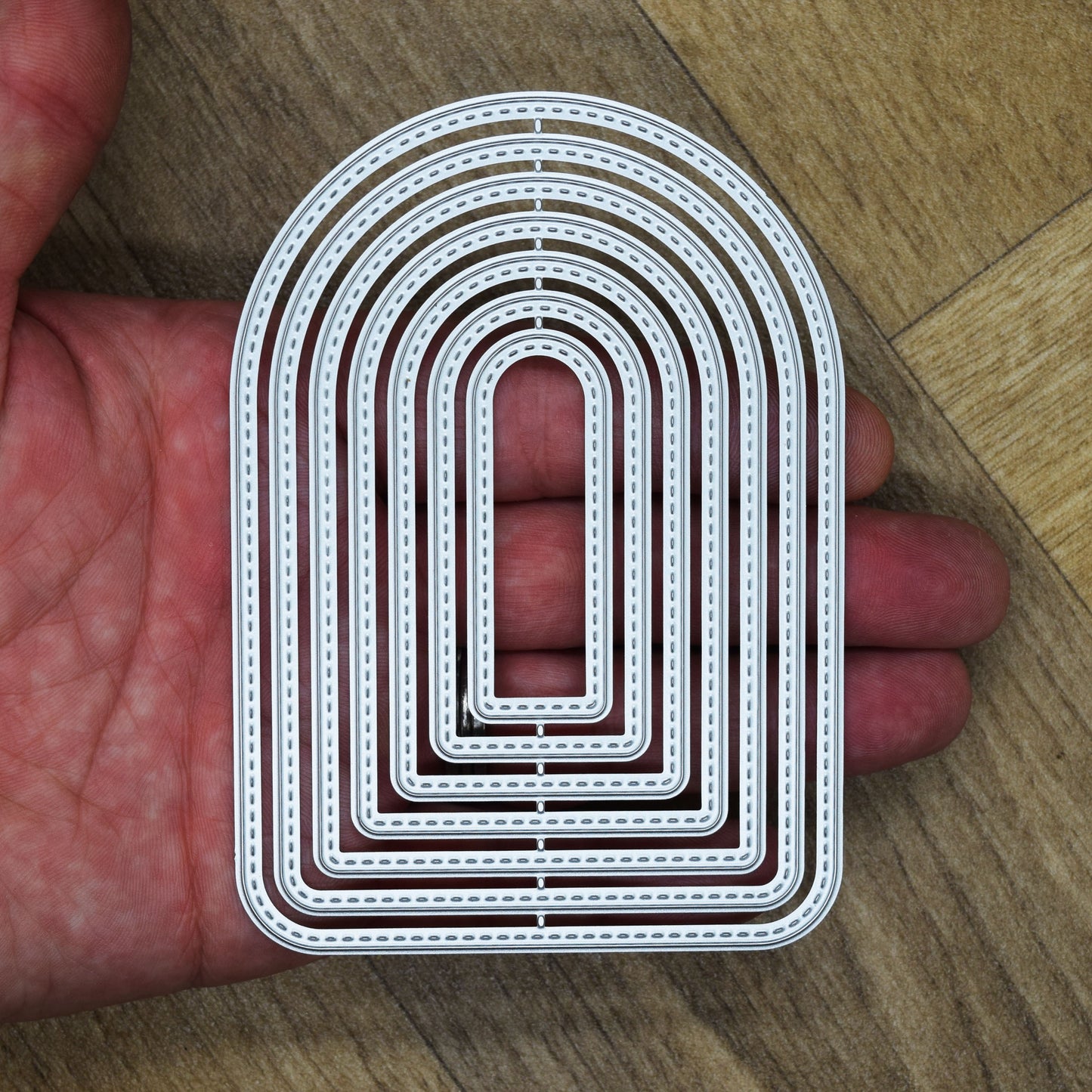 Seven stitched arch nesting metal cutting dies held in a hand to demonstrate the overall size of the set.