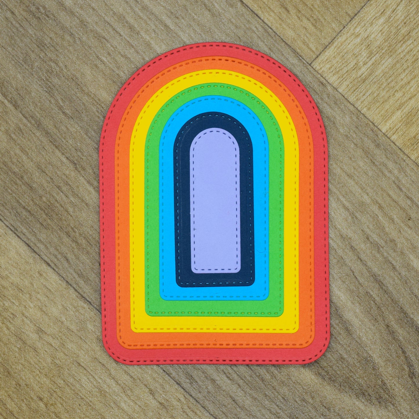 Colourful stitched arch die cuts layered from largest to smallest on a wood-effect background.