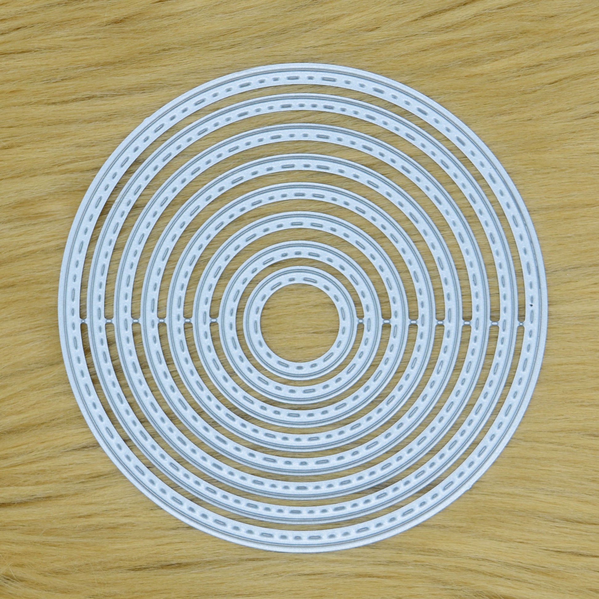 Set of eight stitched circle nesting metal cutting dies displayed together on a tan faux fur background.