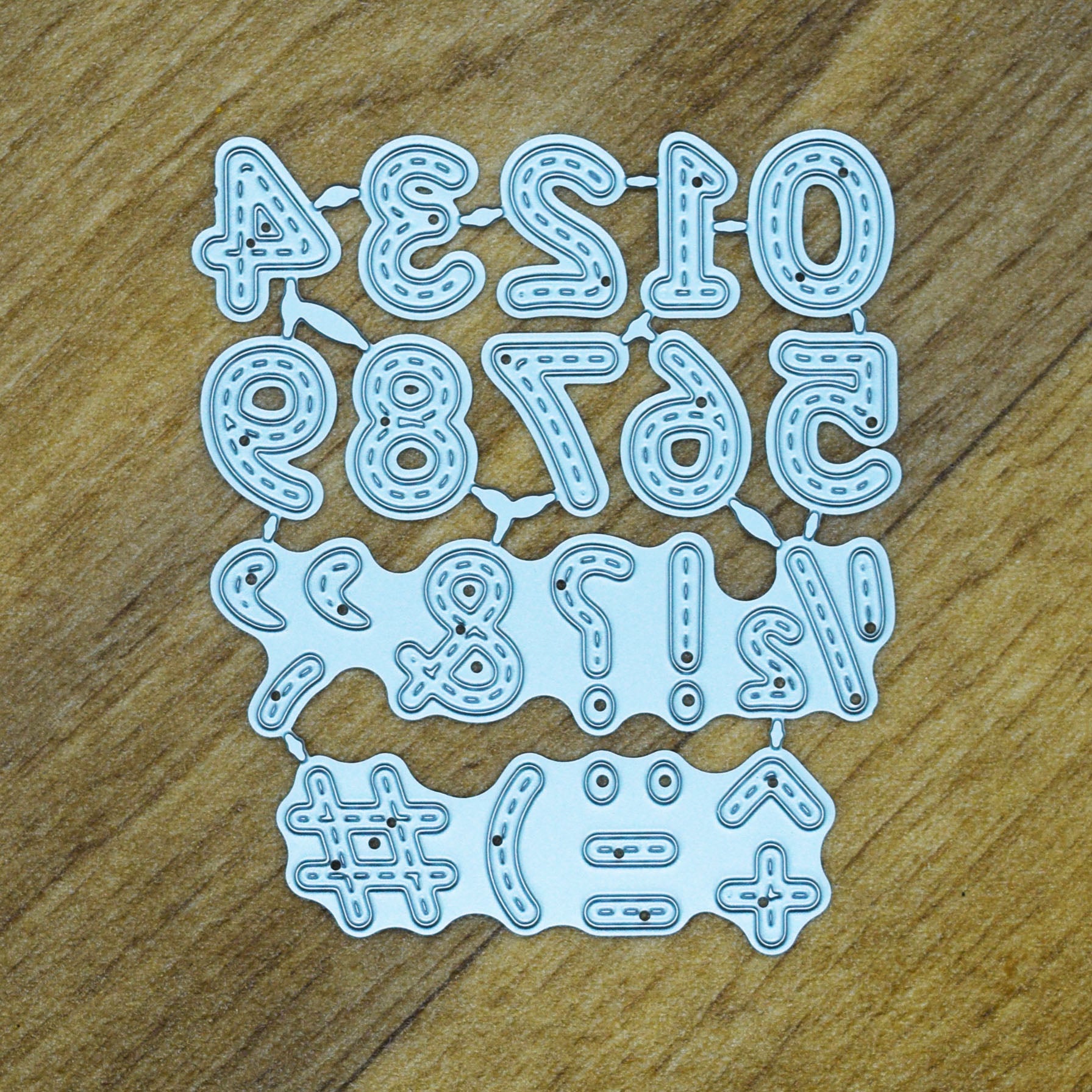 Connected stitched numbers and symbols metal cutting die set displayed on a wood-effect background.