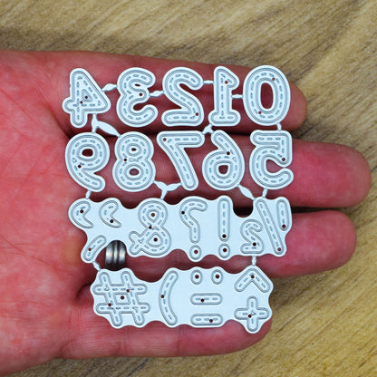 Stitched numbers and symbols metal cutting dies held in a hand to show the overall size of the connected set.