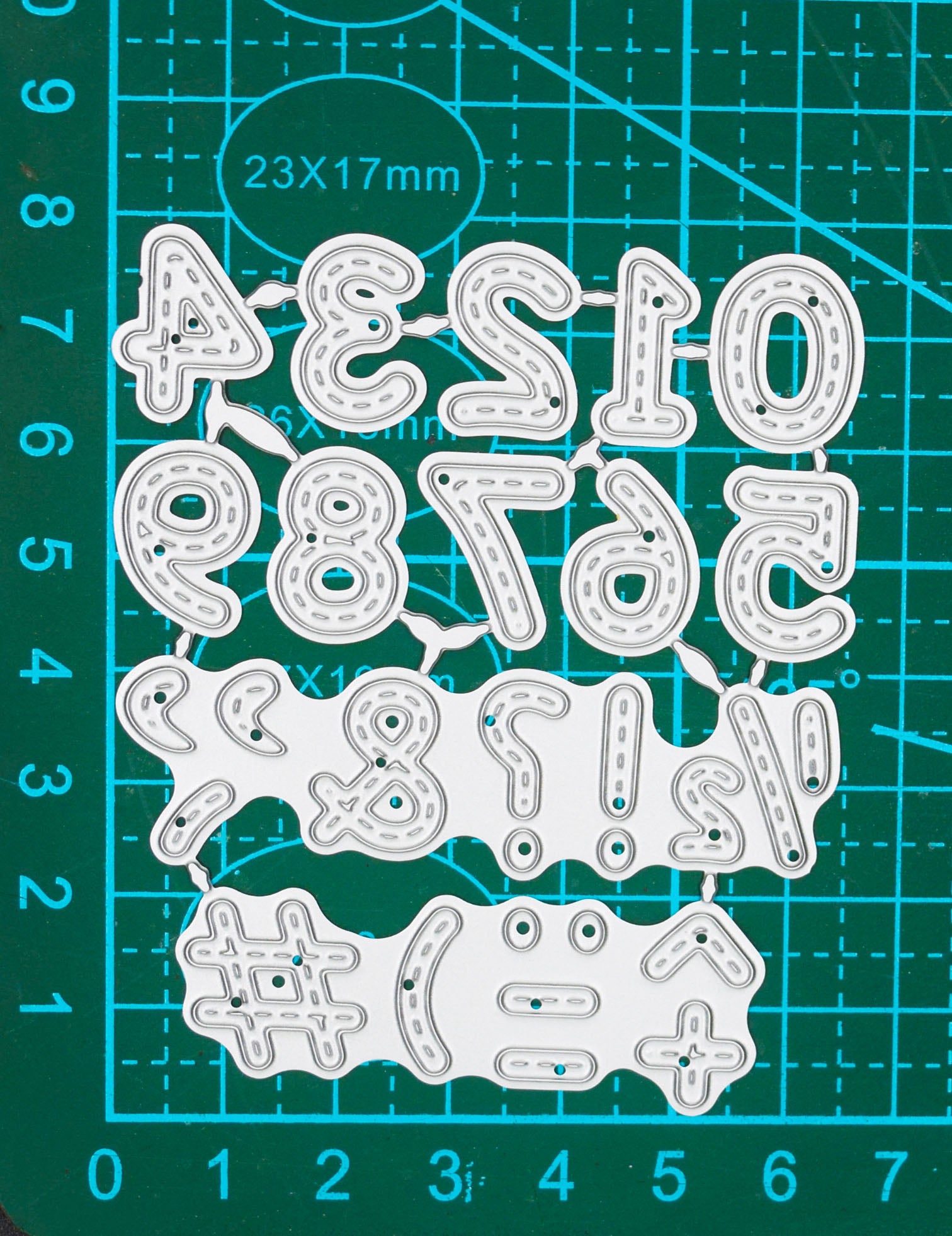Connected stitched number and symbol metal cutting dies displayed on a centimetre cutting mat for size guidance.