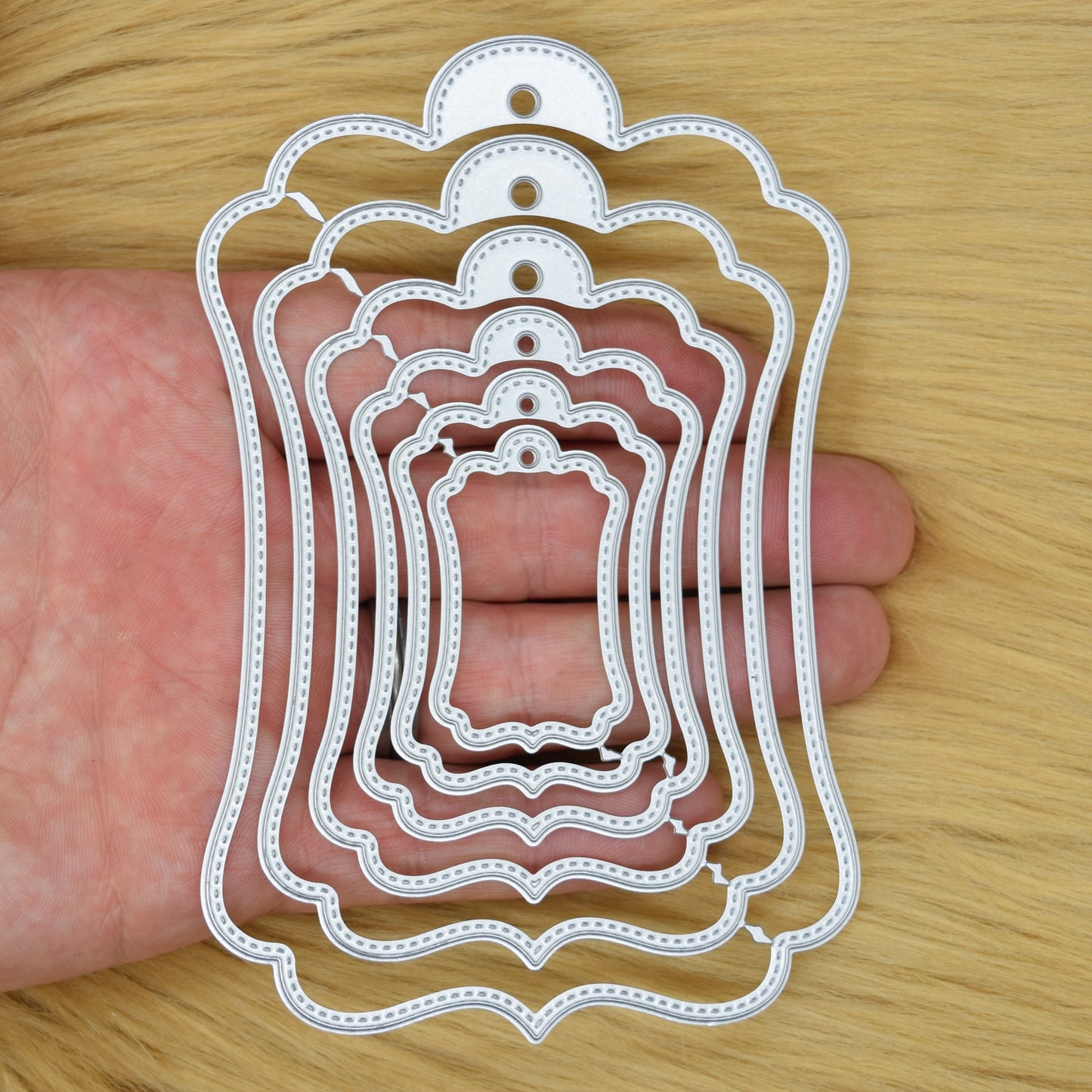 Stitched tag nesting metal cutting dies set shown in hand for size