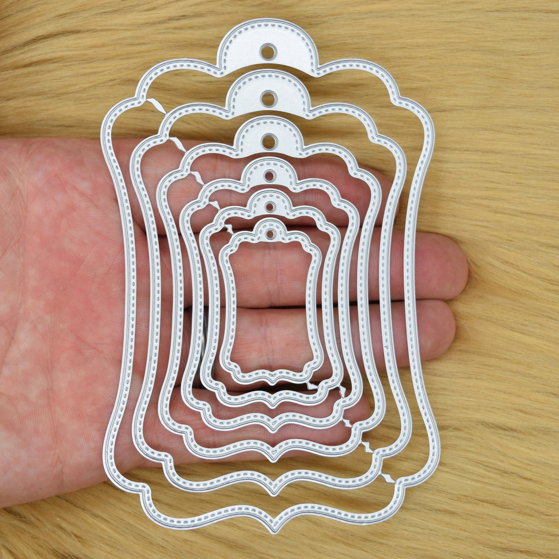 Stitched tag nesting metal cutting dies set shown in hand for size