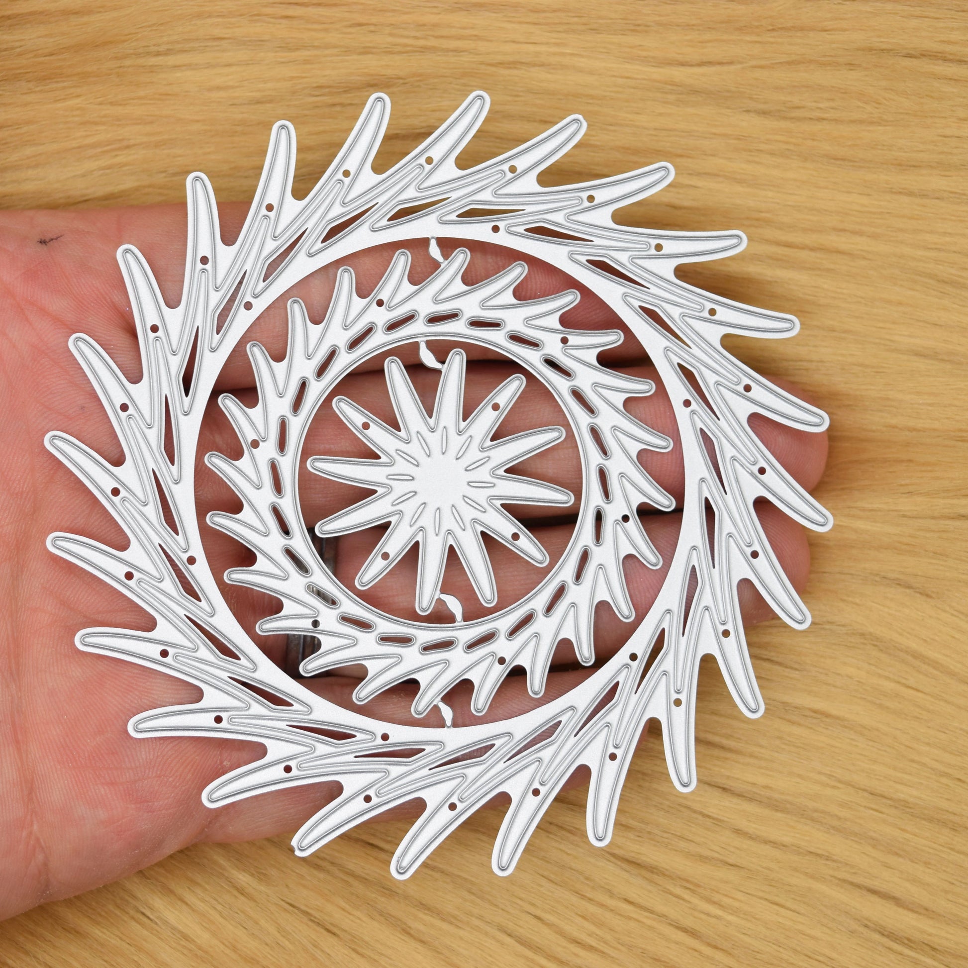 Decorative circular swirl dies shown in hand for scale